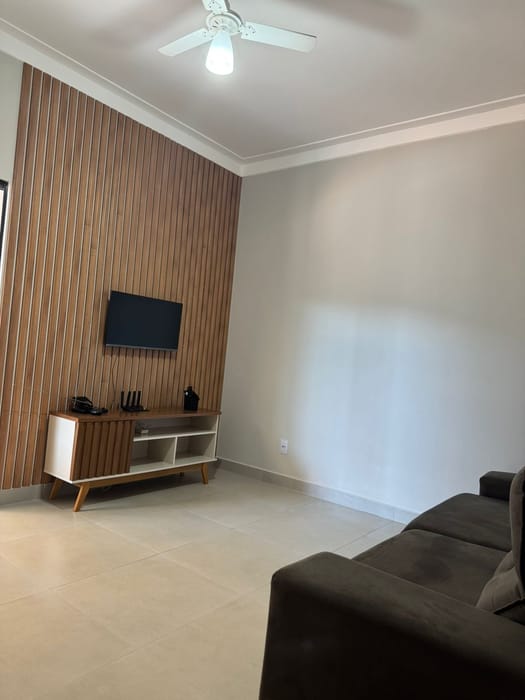 Sala de estar da casa, com TV e painel ripado